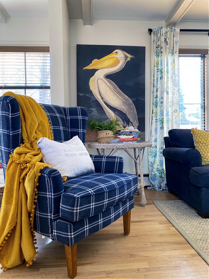 Blue plaid chair with yellow throw and large coastal bird art.