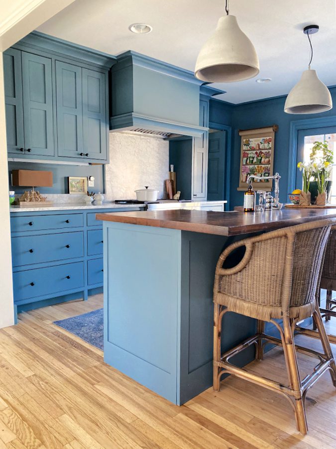A blue kitchen with rattan chairs.
