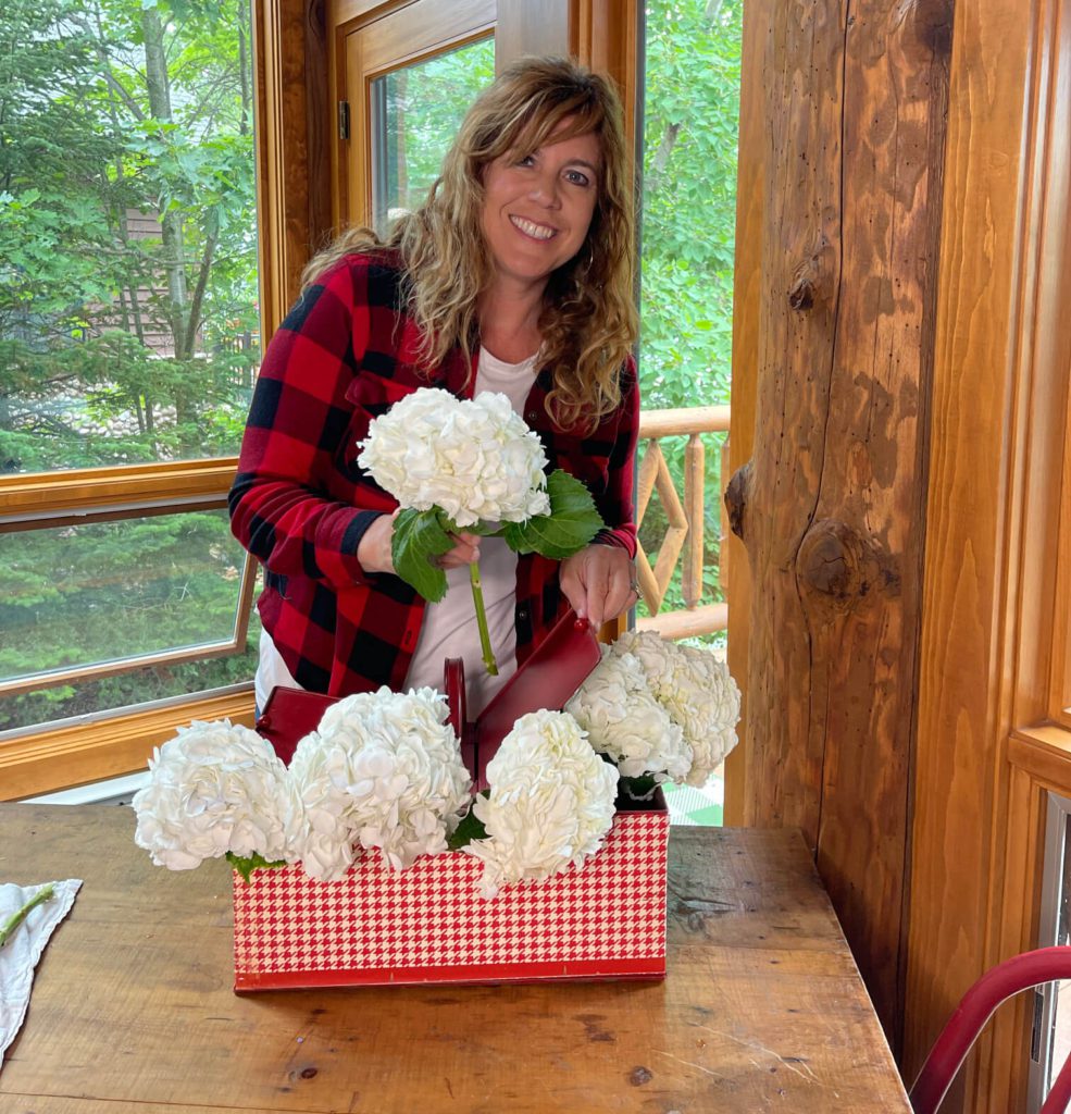 Welcome Home Saturday: Summer Tablespace and Centerpiece Decor | Welcome Home Saturday by popular Alabama lifestyle blog, She Gave It A Go: image of a woman arranging some white hydrangeas in a red and white metal basket. 