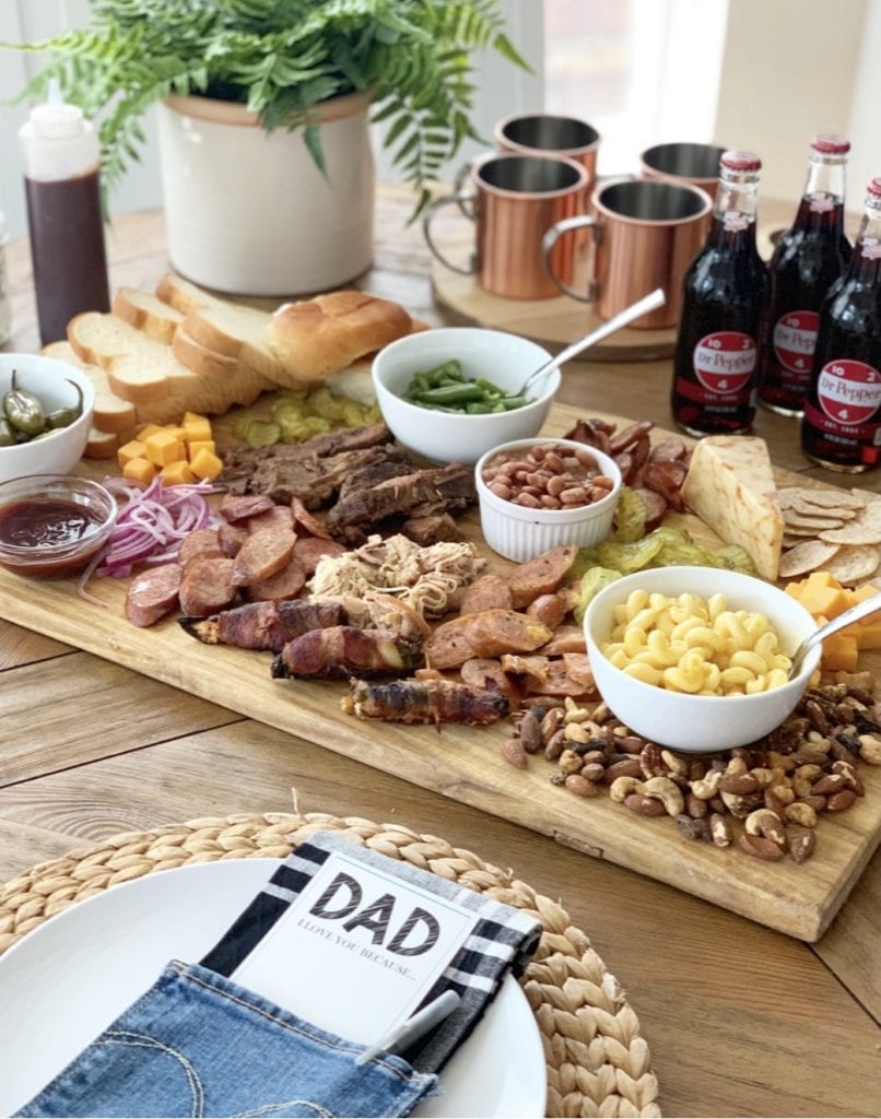 Welcome Home Saturday: BBQ board and printables for dad | Welcome Home Saturday by popular Alabama life and style blog, She Gave It A Go: image of a wooden serving board filled with dried meats, nuts, cheese, crackers, purple onion slices, BBQ sauce, jalapeño peppers, baked beans, Mac n' Cheese, green beans, and slices of bread. 