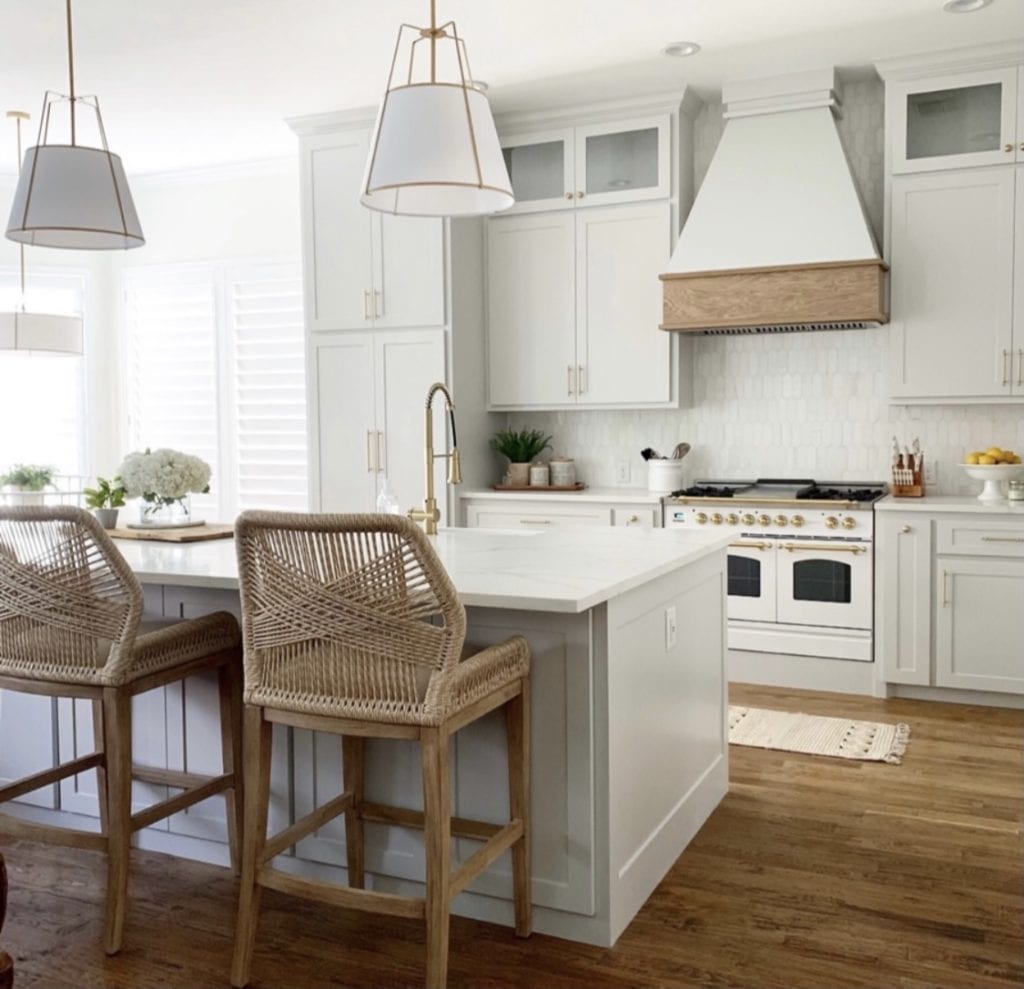 Welcome Home Saturday: Our Kitchen Remodel | Welcome Home Saturday by popular Alabama lifestyle blog, She Gave It A Go: image of a kitchen with white pendant lights, white cabinets, light wood bar stools, white tile backsplash, white gas range stove, and white marble countertops. 