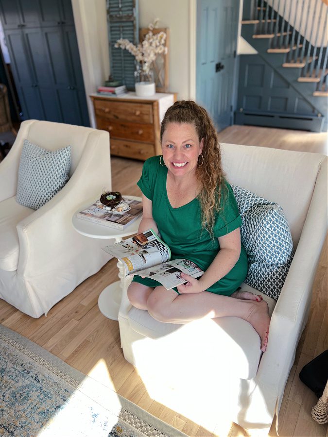 Kelly of the Tattered Pew sitting on a whote chair in a green dress, sharing her Spring home tour 2023.