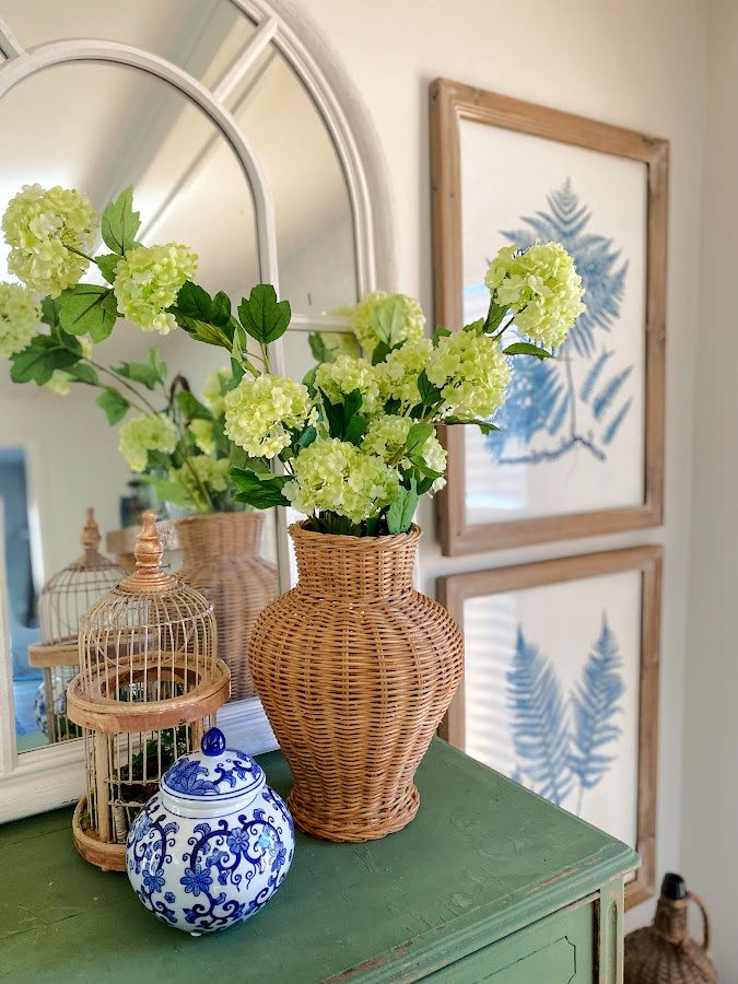 Rattan vase, faux viburnum flowers, mirror and blue and white jar perfect for Spring.