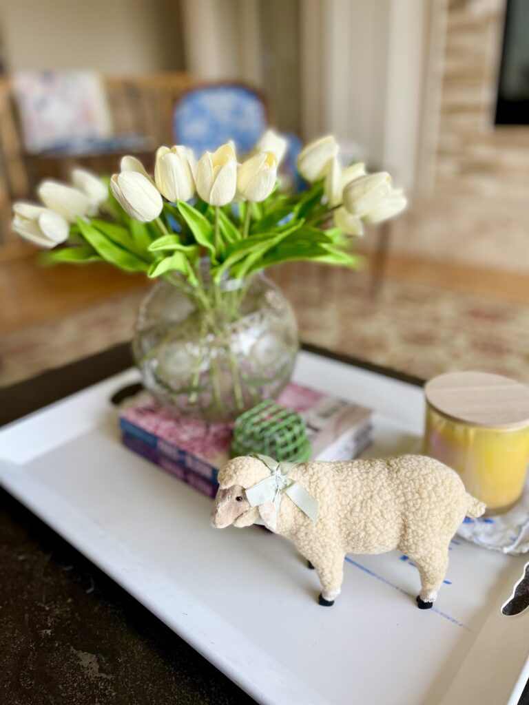 faux white tulips in round vase on a stack of books with lamb figurine