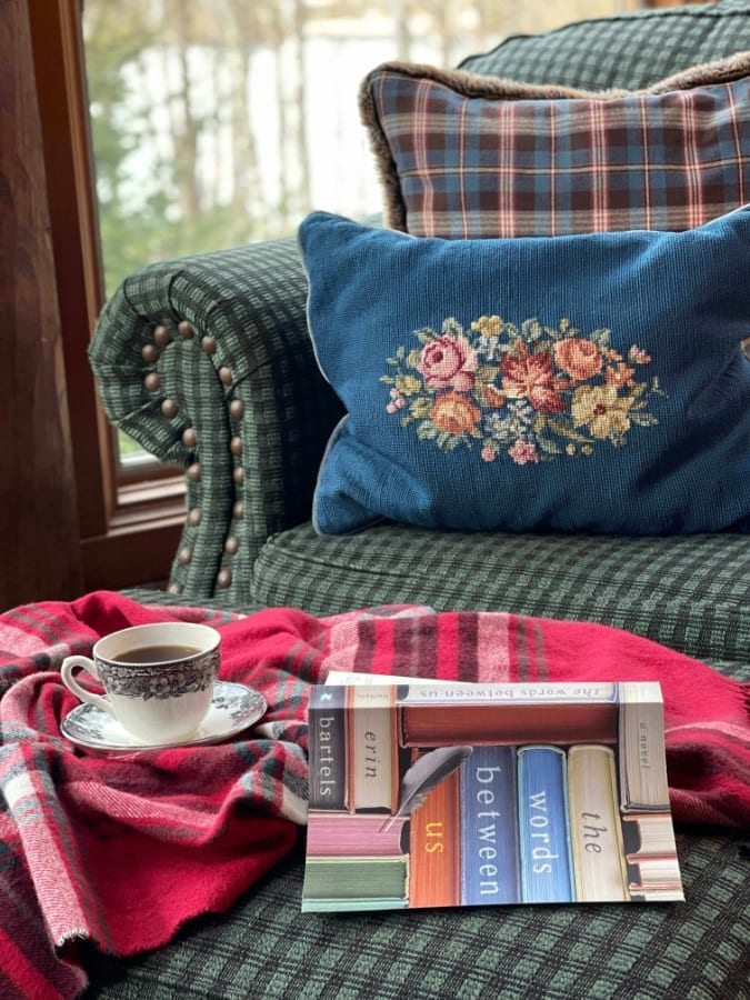Welcome Home Saturday: Interview with author Erin Bartels |Welcome Home Saturday by popular Alabama lifestyle blog, She Gave It A Go: image of a green plaid armchair, embroidered throw pillow, black and white tea cup and saucer, and a copy of The Word Between Us book. 
