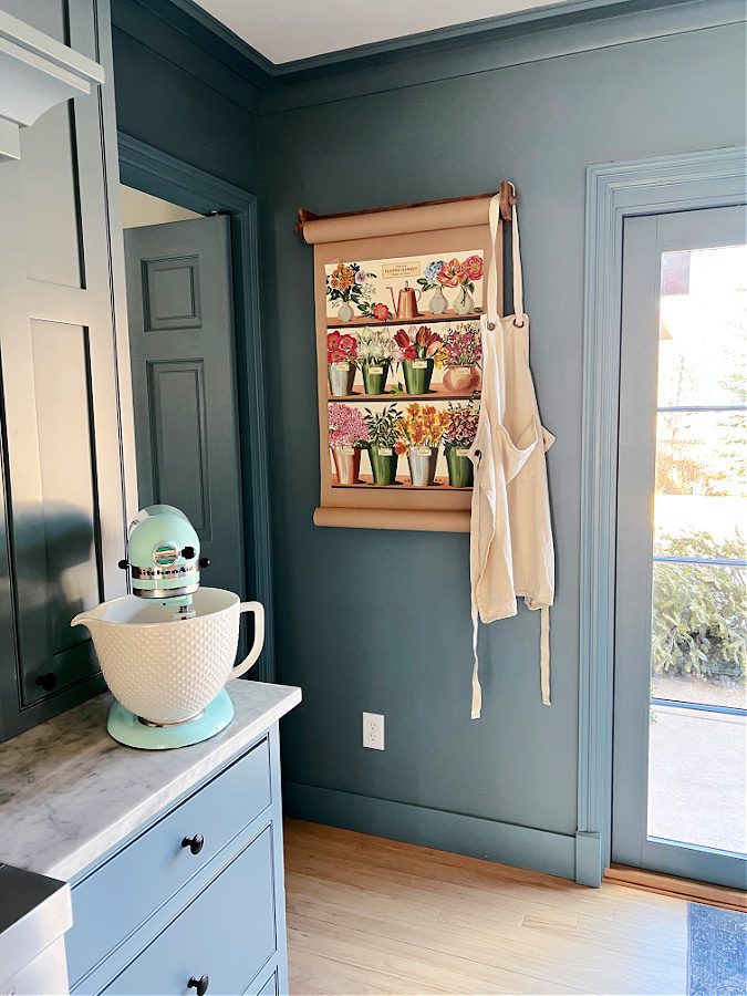 Teal Kitchenaid Mixer on counter and floral poster hanging on wall.