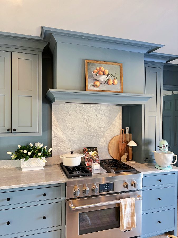 Range and hood in kitchen with fruit art, flowers and marble counters
