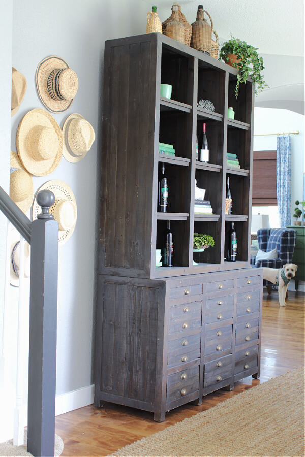 Our Casual Summer Home Tour...come into the dining room! | Welcome Home Saturday by popular Alabama life and style blog, She Gave It A Go: image of a wooden bookcase filled with wine bottle and books next to some woven sun hats hanging on a wall. 