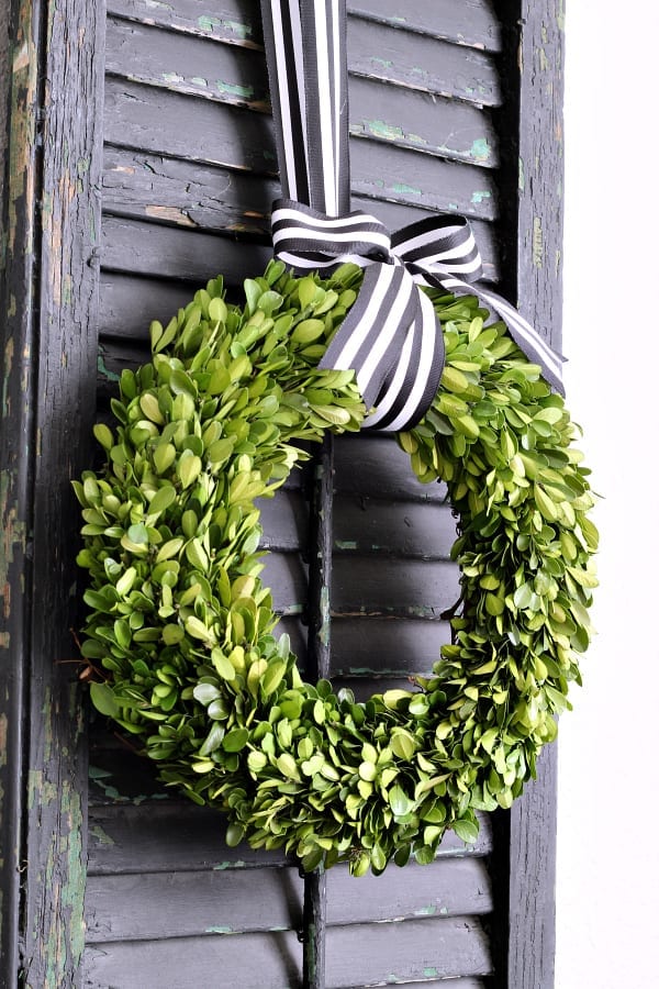 a boxwood wreath hung with black and white ribbon on a black chippy shutter complement each other on the dining room wall.