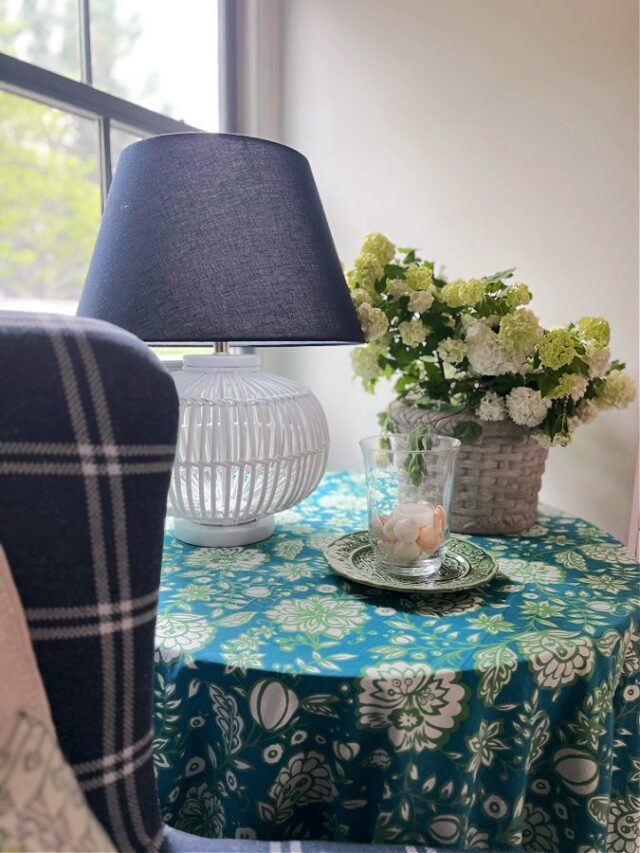 Blue and green Floral covered table with lamp, candle and floral arrangement.