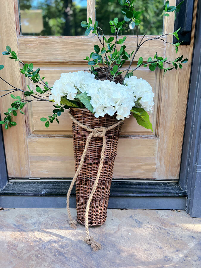 Faux white hydrangeas, greenery stems in a hanging basket. 