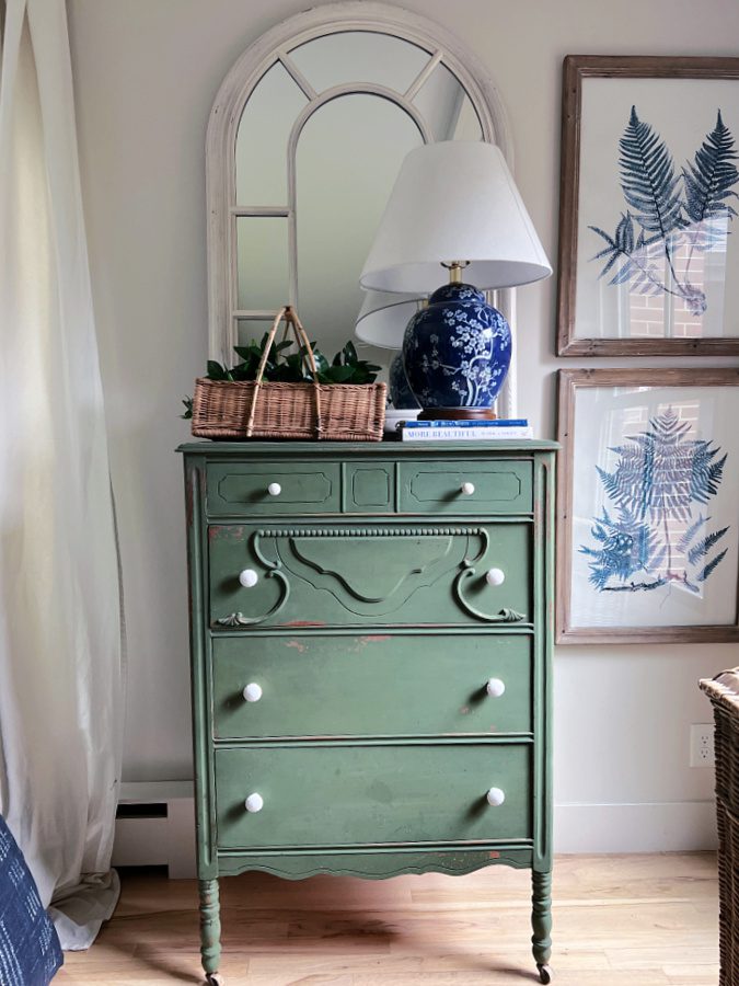 Boxwood green dresser with basket and blue lamp on top. 