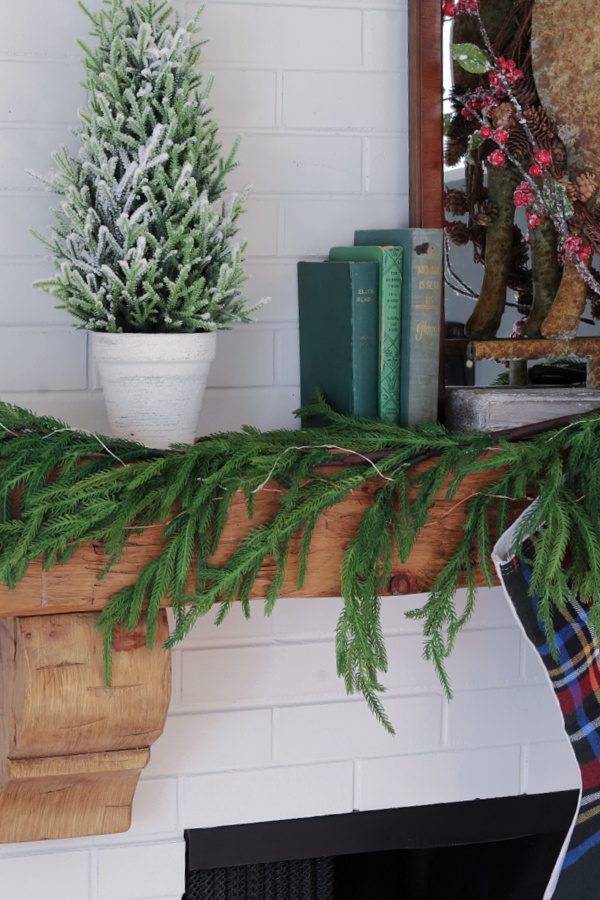 Rustic Christmas mantels include flocked trees, books and garland.