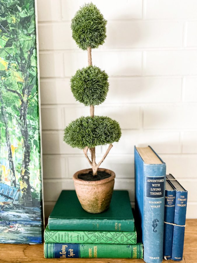A faux topiary stacked on books adds height to a Spring mantel.