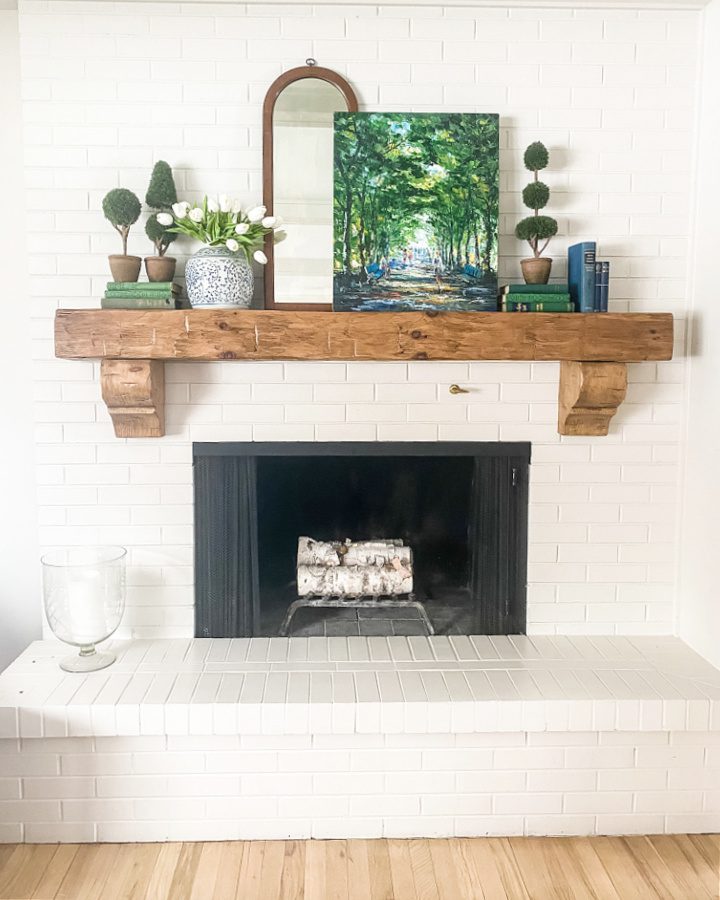 White brick fireplace with a rustic wood beam mantel decorated with blues and greens for Spring.