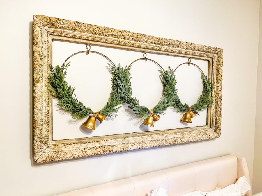 Large vintage frame with three wreaths in the middle above bed.