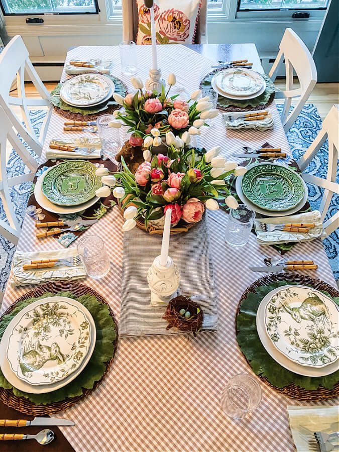 A pretty Easter table set with green and white plates and pops of pink and white flowers.