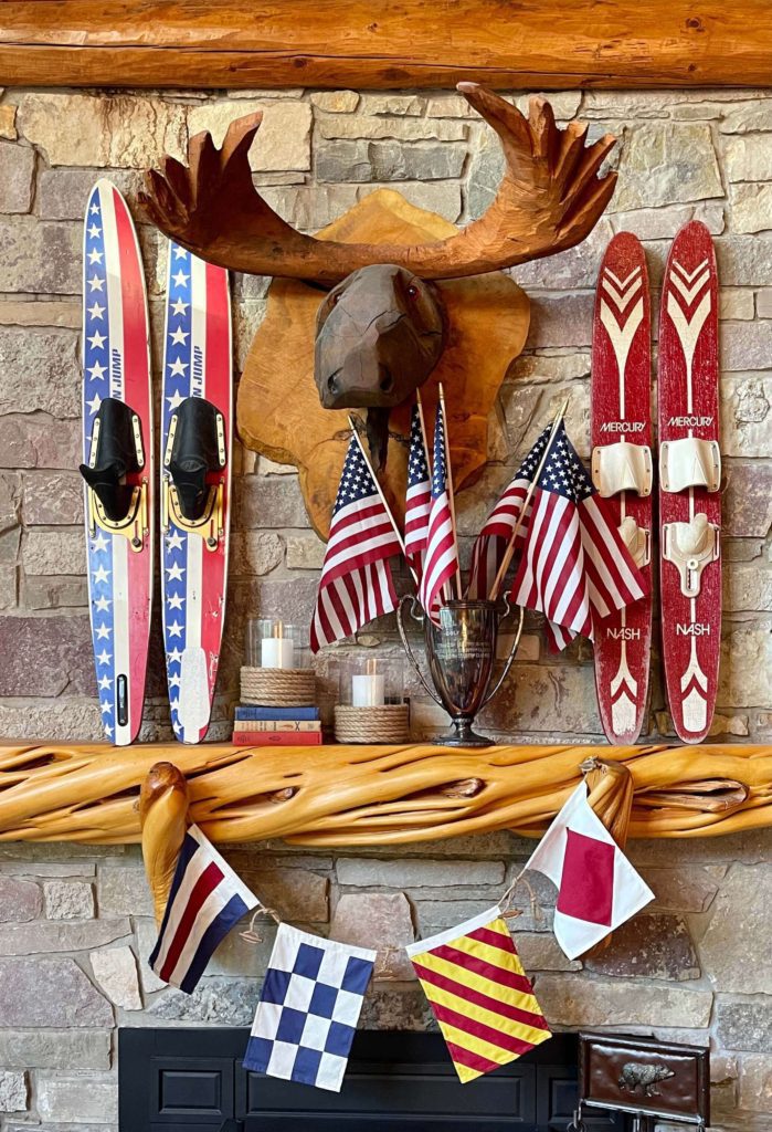 Welcome Home Saturday: Two Summertime Mantels For Timeless Style | Welcome Home Saturday by popular Alabama life and style blog, She Gave It A Go: image of red, white, and blue water skis on a mantle next to a wooden moose head, candle votives wrapped in rope, and a silver trophy cup filled with American flags. 