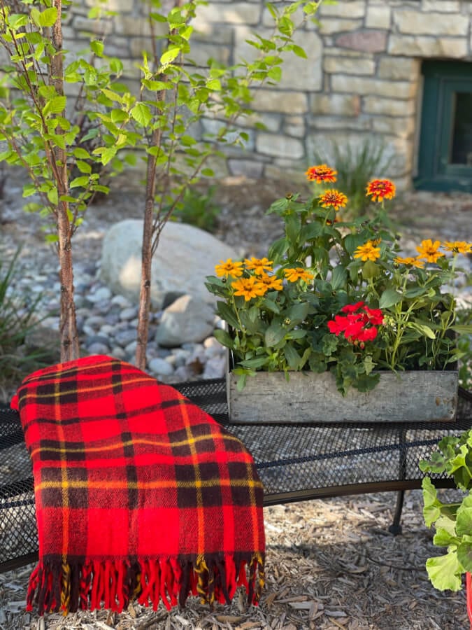 Welcome Home Saturday: Make an Old Garden Bench New With Spray Paint | Welcome Home Saturday by popular Alabama lifestyle blog, She Gave It A Go: image of an old wire bench with a metal planter box filled with flowers and a red, yellow, and black throw blanket resting on top. 