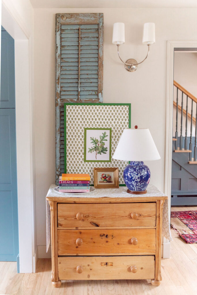 Entry dresser with lamp, green block print art, stacked books and blue shutter