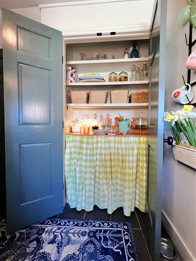 Our storage pantry decorated for Spring with green gingham curtain and baskets on shelves. 