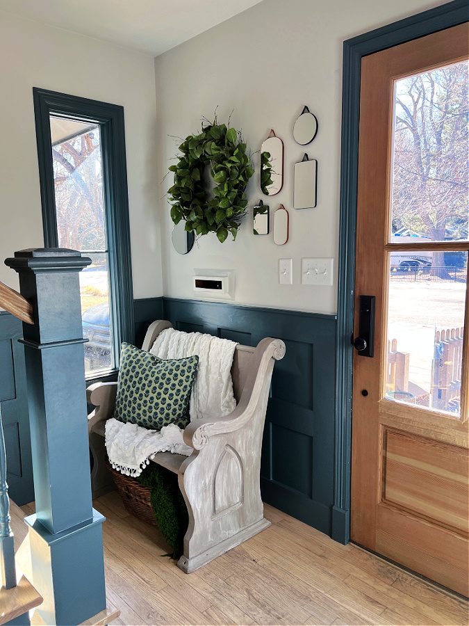 Little pew in entry of Spring Home Tour 2023 with mirrors above it and green wreath. At the bottom of the stairwell.