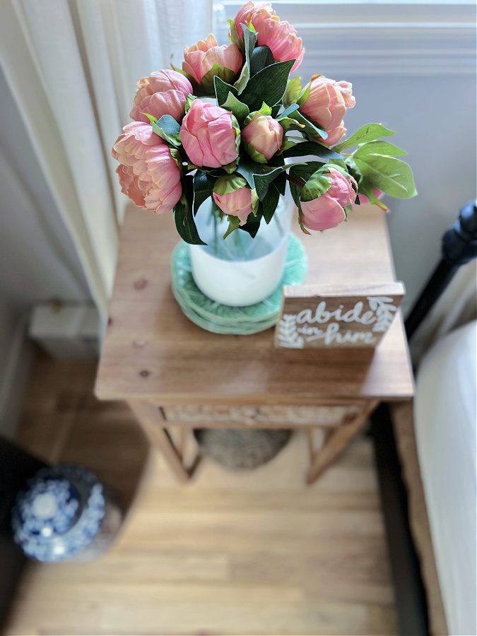 Overhead view of faux pink peonies in white dipped vase and set on a stack of green plates.