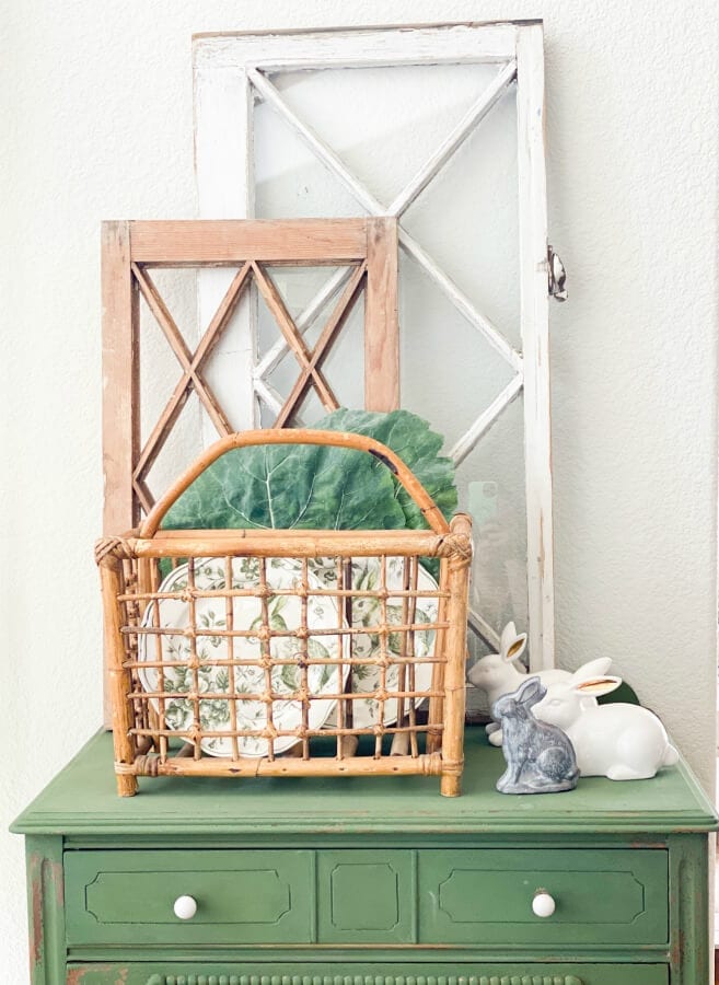 Wicker magazine rack with plates inside it with two vintage doors behind it.