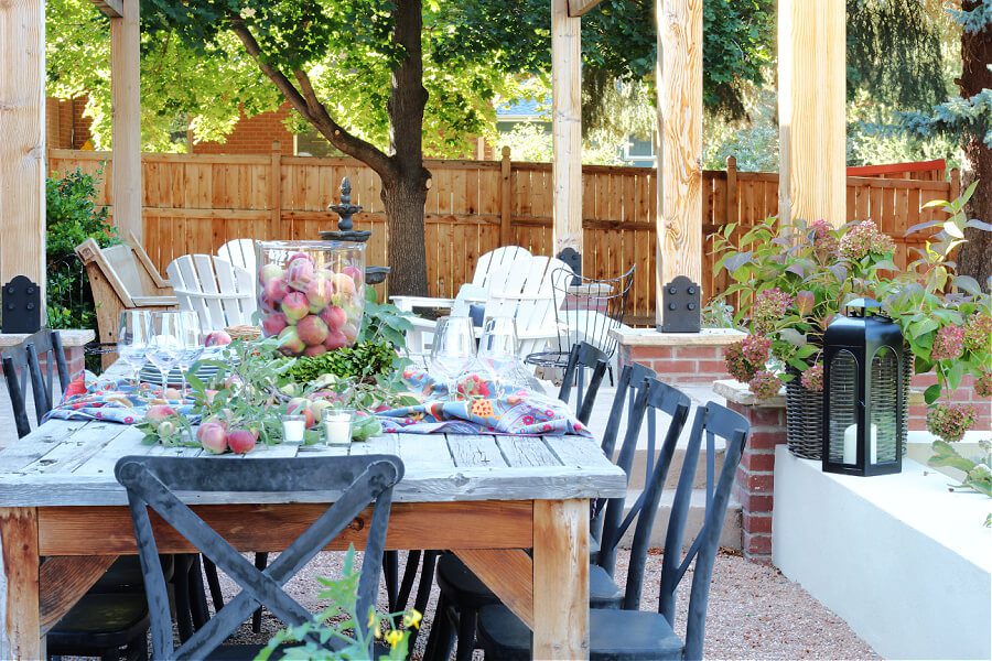 Black chairs, long wooden table, under an outdoor pergola.
