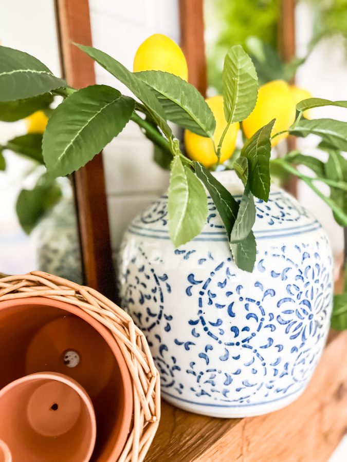 A simple summer mantel with lemon stems and ginger jar canister against white brick.