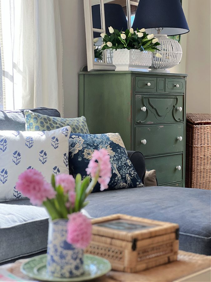 Our Spring family room with pink flowers in a blue pitcher, blue and white pillows and a green painted dresser.