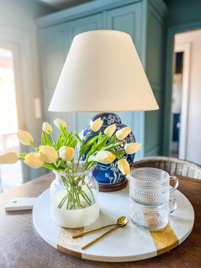 Faux tulips on white charcuterie board, with glasses and lamp.