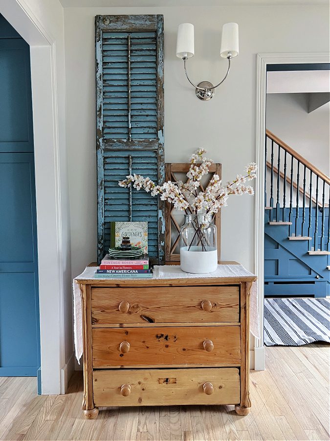 pine dresser with large blue shutter above it. A vase full of  faux cherry blossom stems.