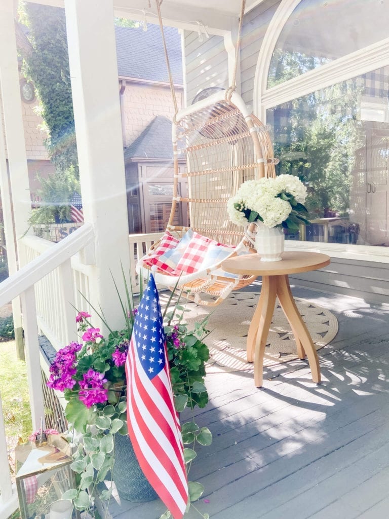 Welcome Home Saturday: Cottage Summer Home Tour | Welcome Home Saturday by popular Alabama life and style blog, She Gave It A Go: image of a front porch decorated with a hanging rattan swing, woven circular rug, and wooden table with a white vase filled with white flowers resting on it. 