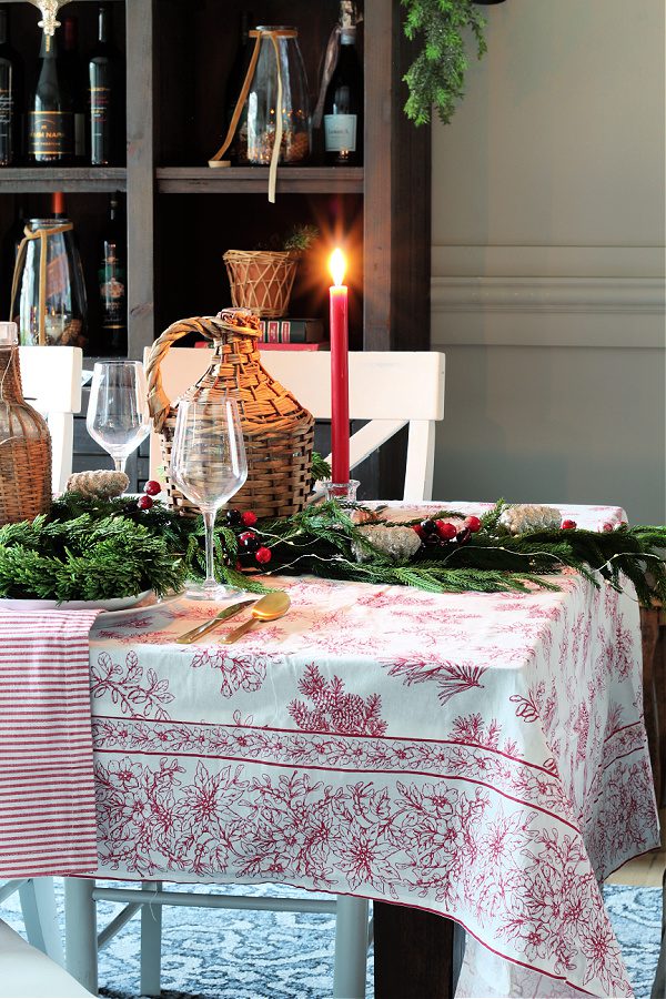 Wicker demi johns, candles and a botanical April Cornell table cloth add elegant touches to this dining room for Christmas.