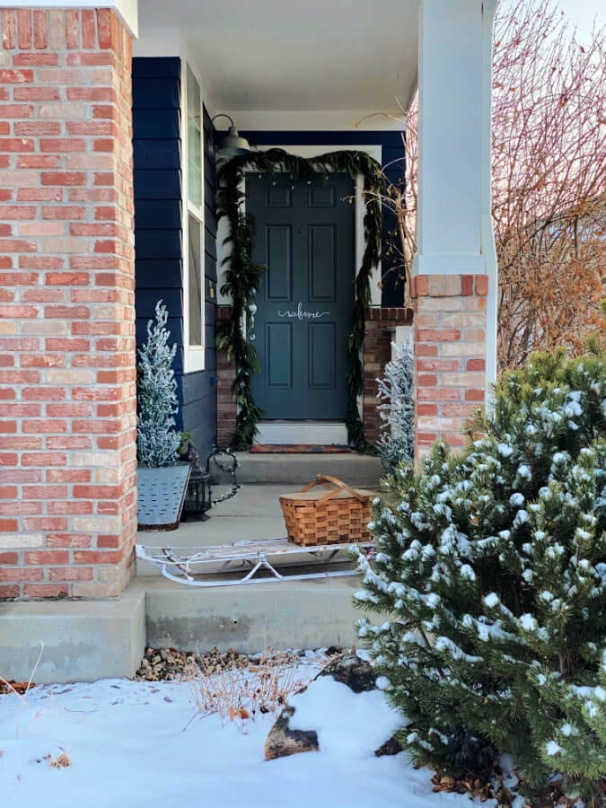 A vintage sled, old basket and live greenery greets you as you enter our winter porch!